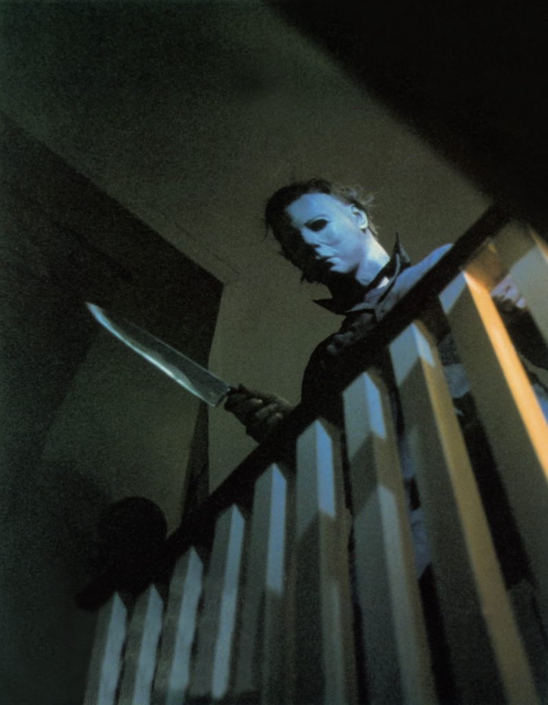 Michael Myers schaut das Geländer herab, ein riesiges Messer in der Hand - Halloween - Die Nacht des Grauens