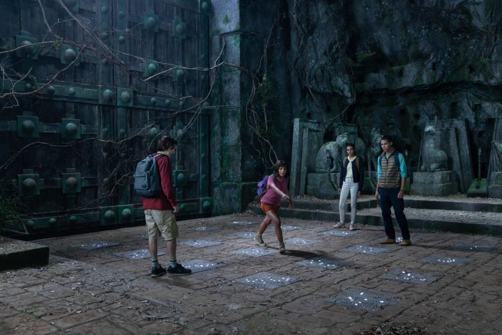 Dora und ihre Freunde stehen vor einem großen Tor auf leuchtenden Steinplatten. Dora zeigt auf eine der Platten. Dora und die goldene Stadt ©Paramount Pictures