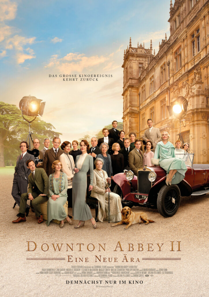 Auf dem Filmplakat zu Downton Abbey 2: Eine neue Ära versammelt sich der gesamte Cast vor einem großen Gutshaus, im Hintergrund sind zwei Scheinwerfer zu erkennen. Dazu sieht man ein Automobil aus der Zeit der 1920er.