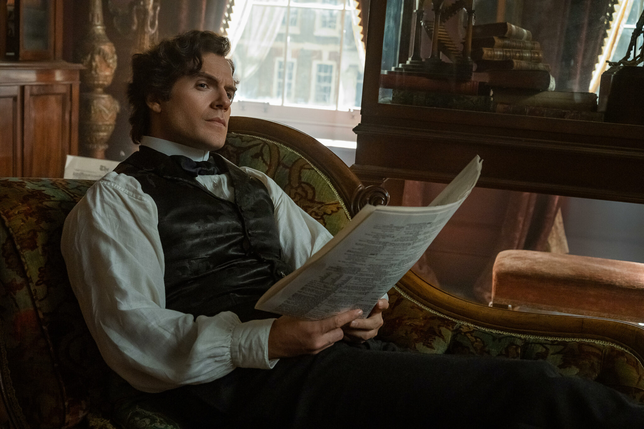 Henry Cavill ist wieder Sherlock Holmes mit edlem Outfit auf einer Bank mit Zeitung in der Hand.