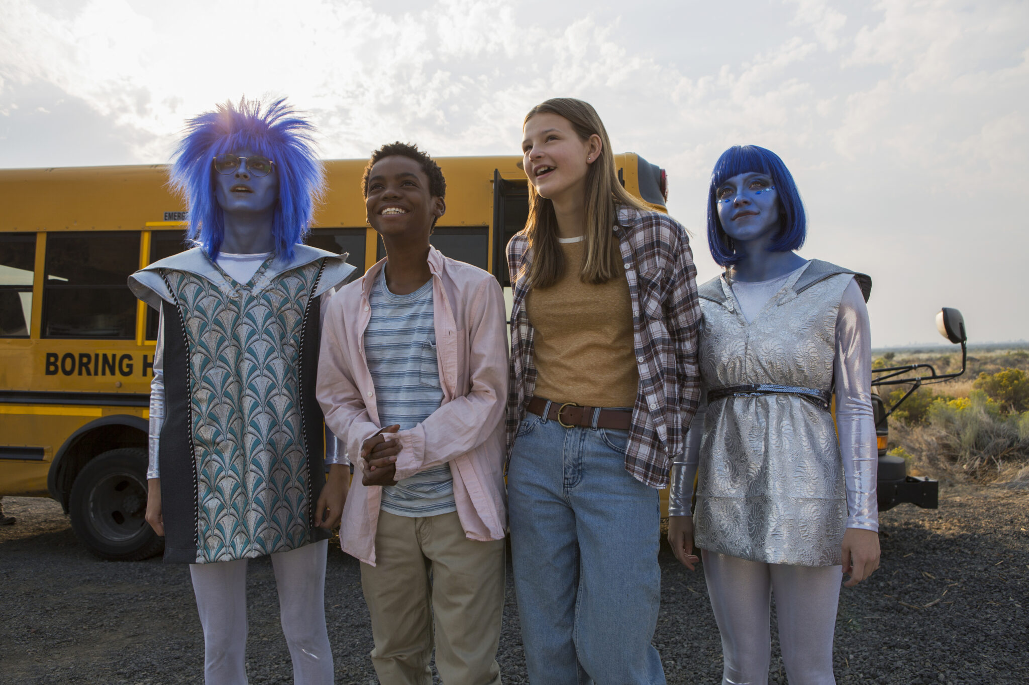 Vier Teenager vor einem gelben Schulbus. Zwei als Aliens blau geschminkt, zwei in normaler Alltagskleidung. Coming of Age-Serien Tipps