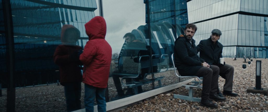 Der Junge, gespielt von Sevastian Bugaev, Igor, gespielt von Vladimir Vdovichenkov, und ein Freund spiegeln sich in den Glasfassaden der Gebäude.