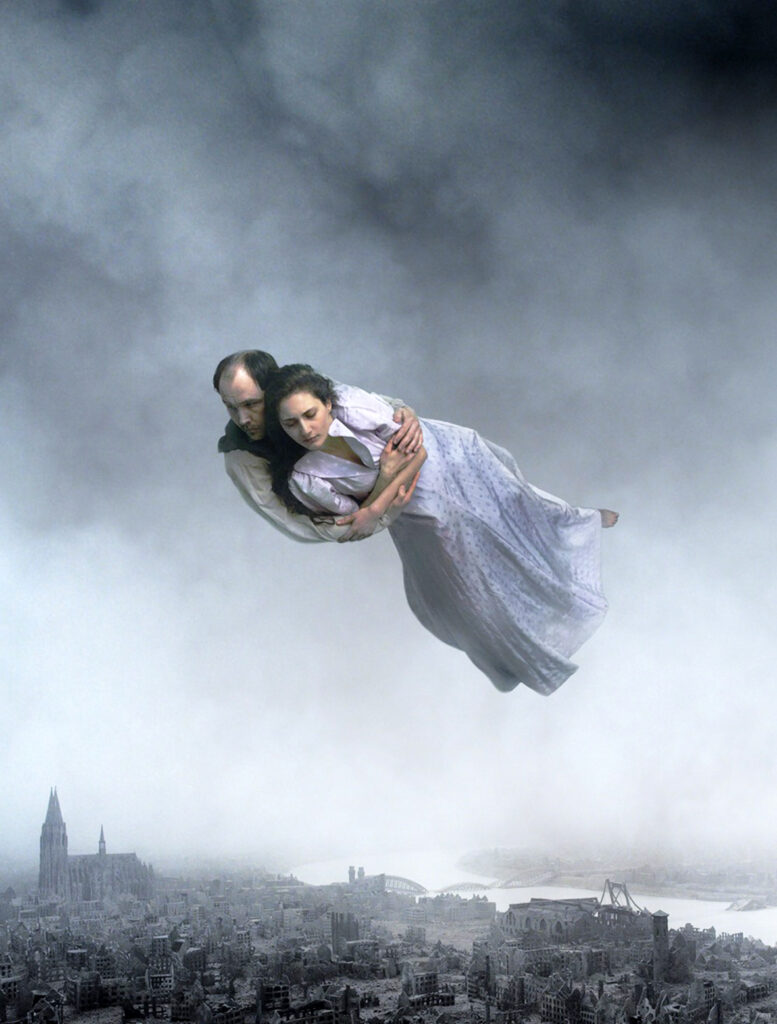 Ein Paar schwebt fest umschlungen über einer zerstörten Stadt in "Über die Unendlichkeit"