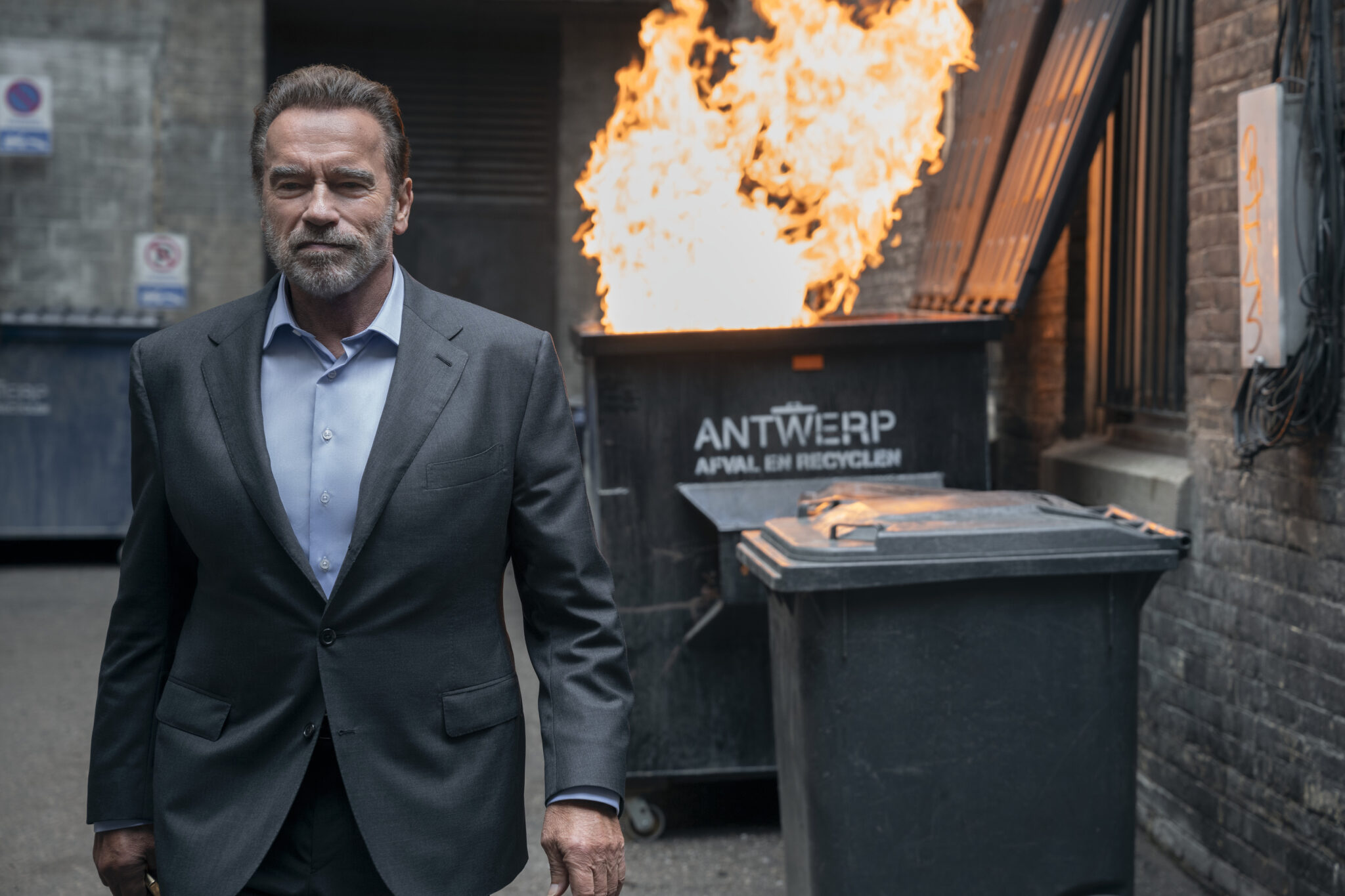 Arnold Schwarzenegger als Luke Brunner vor einer brennenden Papiertonne im Anzug