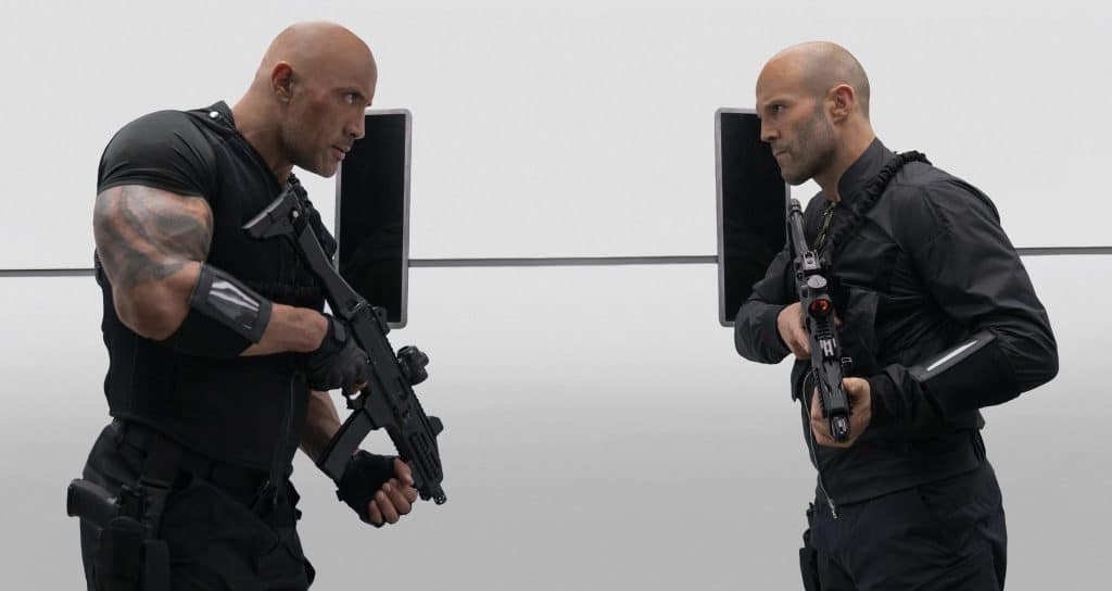 Dwayne The Rock Johnson und Jason Statham aus Fast & Furious Hobbs & Shaw stehen sich bewaffnet gegenüber und starren sich wütend an.
