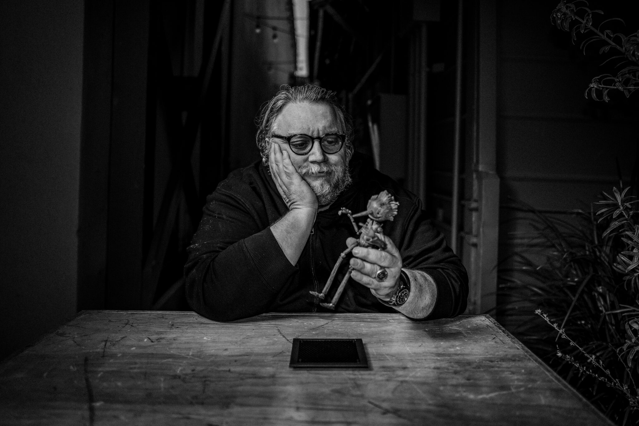 Die Schwarzweißaufnahme zeigt Guillermo del Toro an einem Tisch sitzend mit einer Holzpuppe in der Hand.