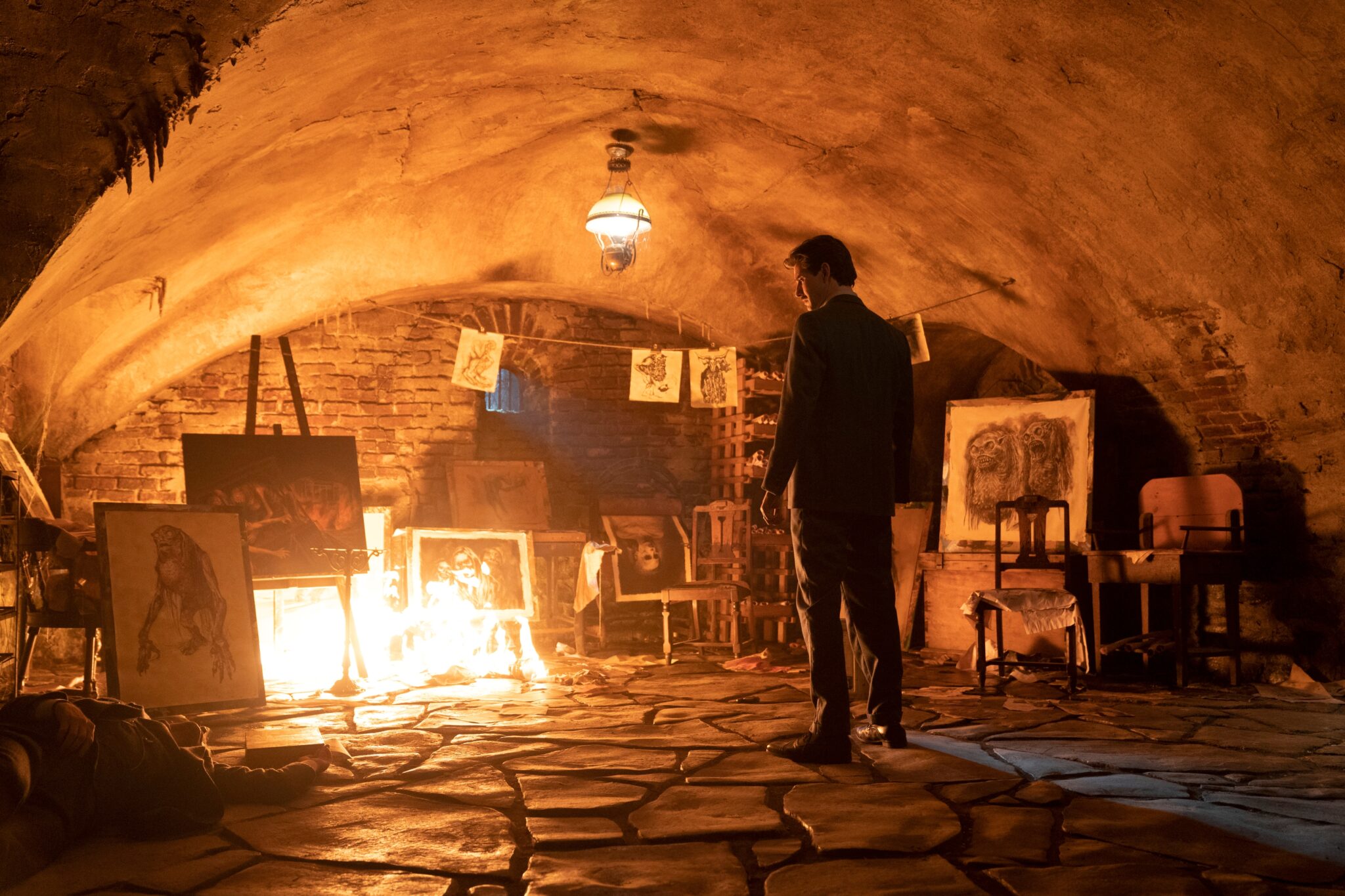 Ben Barnes in einem Keller vor einigen Bildern. links hat sich ein Feuer entzündet und erhellt das dunkle Zimmer. Cabinet of Curiosities