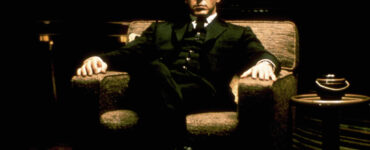 Auf dem Bild erkennt man Michael Corleone im Anzug, wie er selbstbewusst auf einem Sessel sitzt - Der Pate-Trilogie