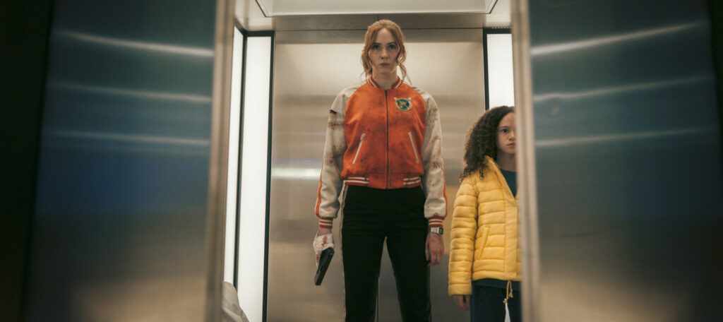 Karen Gillan steht, eine Pistole an ihre Hand geklebt, mit Chloe Coleman an einem Aufzug - Gunpowder Milkshake.