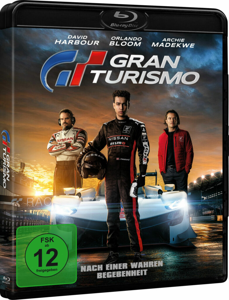 Auf dem Cover zum Gran Turismo Film sind drei Männer zu sehen. Einer steht zentral vor einem Rennauto mit leuchtenden Scheinwerfern. Die anderen beiden stehen jeweils links und rechts neben dem Auto.