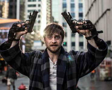 Daniel Radcliffe in Guns Akimbo mit erhobenen Händen, an den jeweils eine Waffe festgeschraubt ist