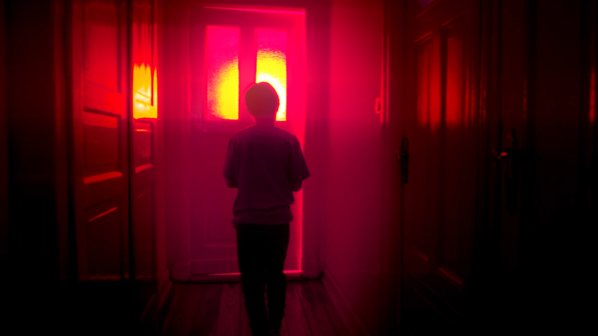 Ein kleiner Junge, der sich mit dem Rücken zur Kamera im Flur eines Hauses der Haustür nähert, durch die von außen rotes Licht hereindringt, ist in "Hager" zu sehen.