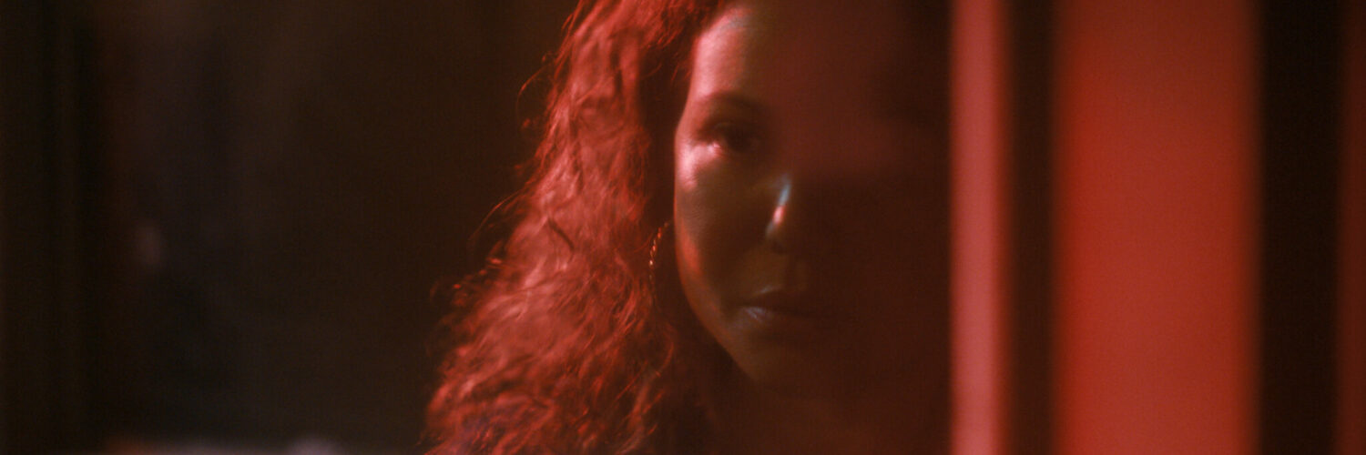 Im Halbschatten des Rotlichts sieht man Dolores Roach hinter einer Fensterscheibe - Neu bei Prime im Juli 2023