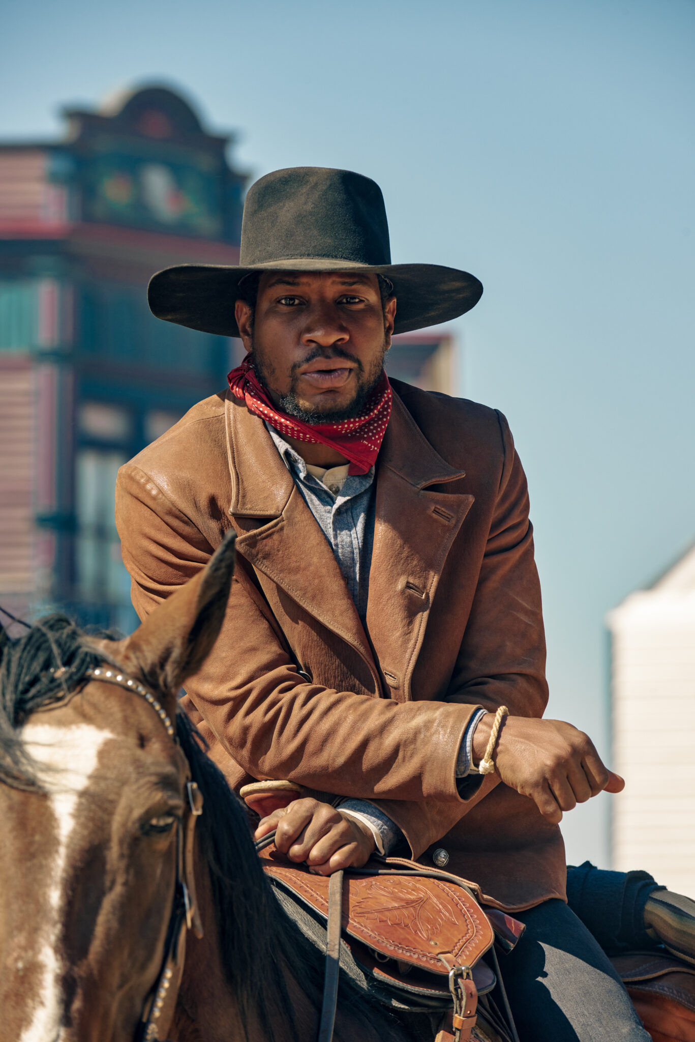 Jonathan Majors als Nat Love. Er sitzt auf einem Pferd, trägt braune Lederjacke samt dunklem Hut und rotem Halstuch.