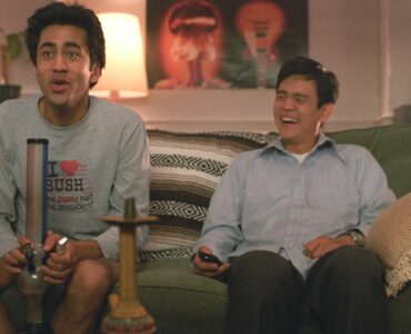 Harold und Kumar sitzen im Wohnzimmer auf der Couch und ziehen an einer Bong. Dabei haben sie eine Menge Spaß.