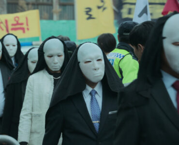 Fanatiker mit weißen Masken marschieren in Hellbound durch die Straßen
