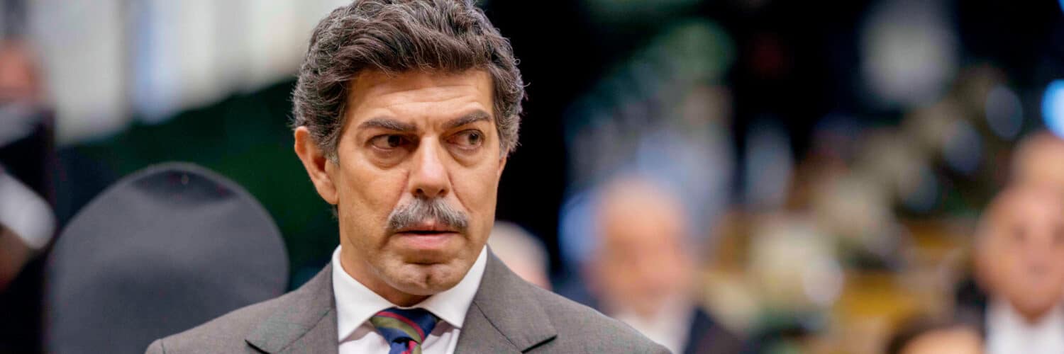 Tommaso Buscetta (Pierfrancesco Favino) steht in Il Traditore - Als Kronzeuge gegen die Cosa Nostra in grauem Anzug und blau-rot-gold-gestreifter Krawatte vor Gericht.
