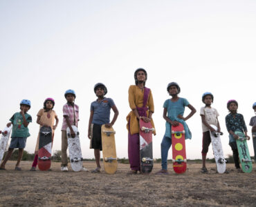 Die Jugendlichen des indischen Dorfes stehen nebeneinander jeweils mit Helm und Skateboard in der Hand.