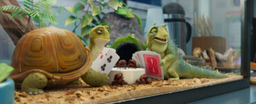 Eine Schildkröte und eine Echse sitzen in einem Terrarium. Sie spielen Karten.