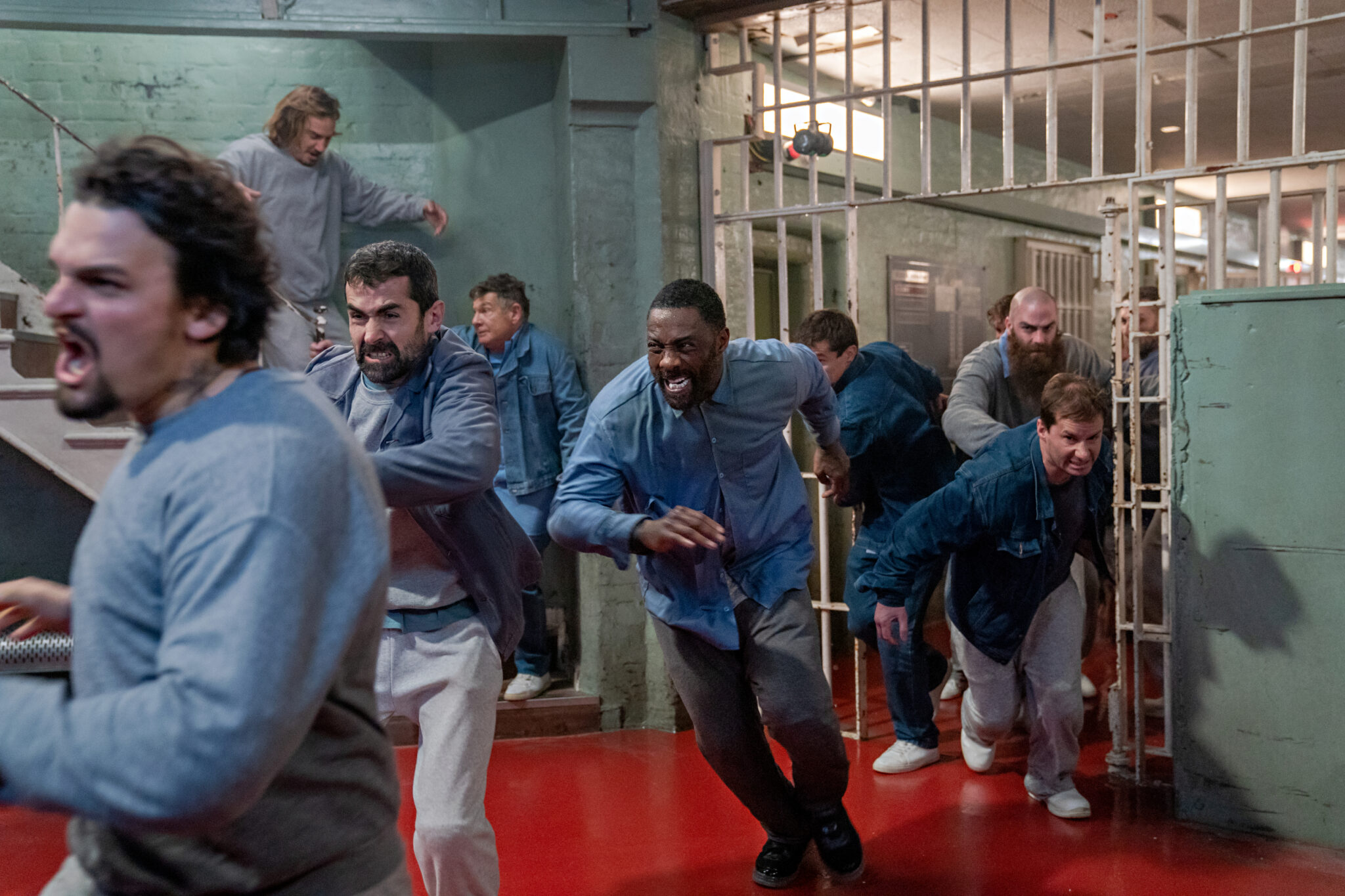 Luther rennt grimmig blickend zwischen anderen Häftlingen durch einen Gefängnissaal.