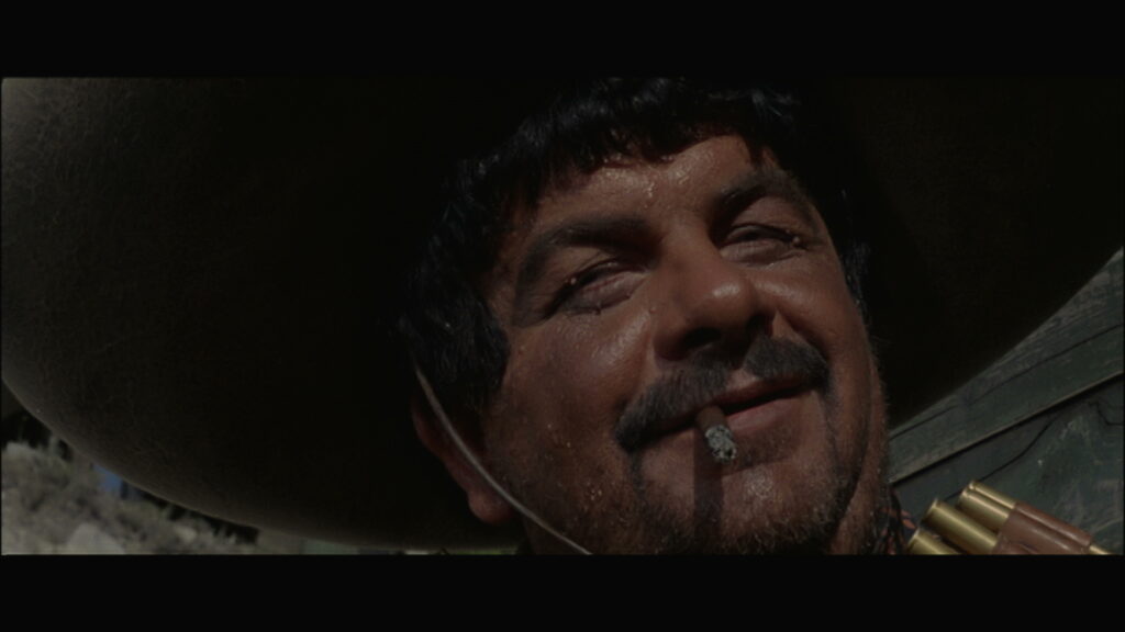Der mexikanische Bandenboss General Porfirio, gespielt von Franco Cobianchi, lacht in der lange Tag der Rache mit Zigarre im Mund über ein ein Opfer.