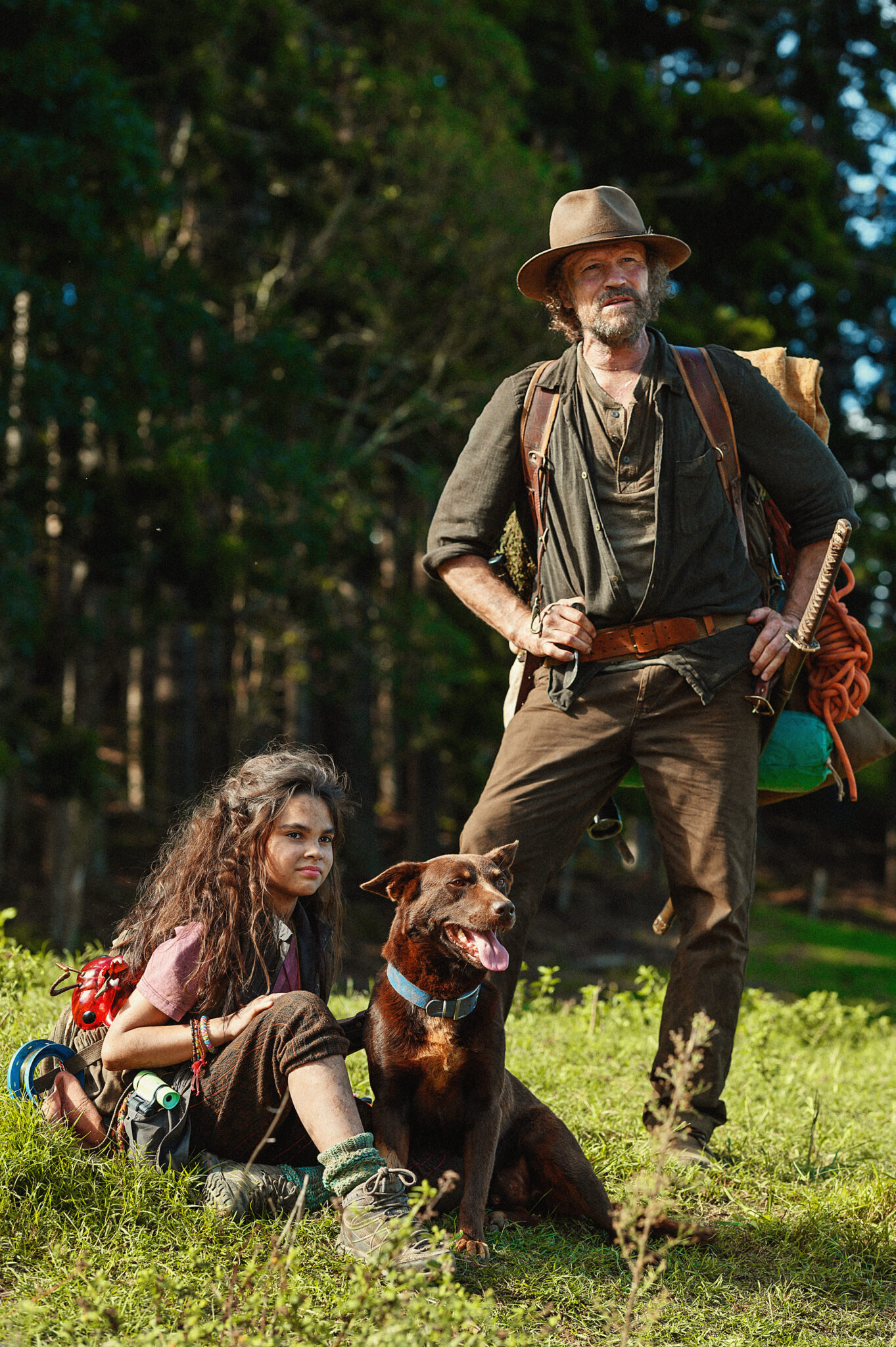 Auf einer Wiese sitzt Minnow (Ariana Greenblatt) mit einem Hund. Neben ihr steht Clyde (Michael Rooker), der eine olivgrüne Jacke und eine braune Hose trägt und auf dem Kopf einen Cowboyhut trägt.