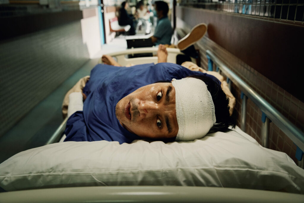 Ein am Kopf bandagierter Mann liegt auf einer Krankenhausbahre und blickt panisch nach oben - Fantasy Filmfest 2023
