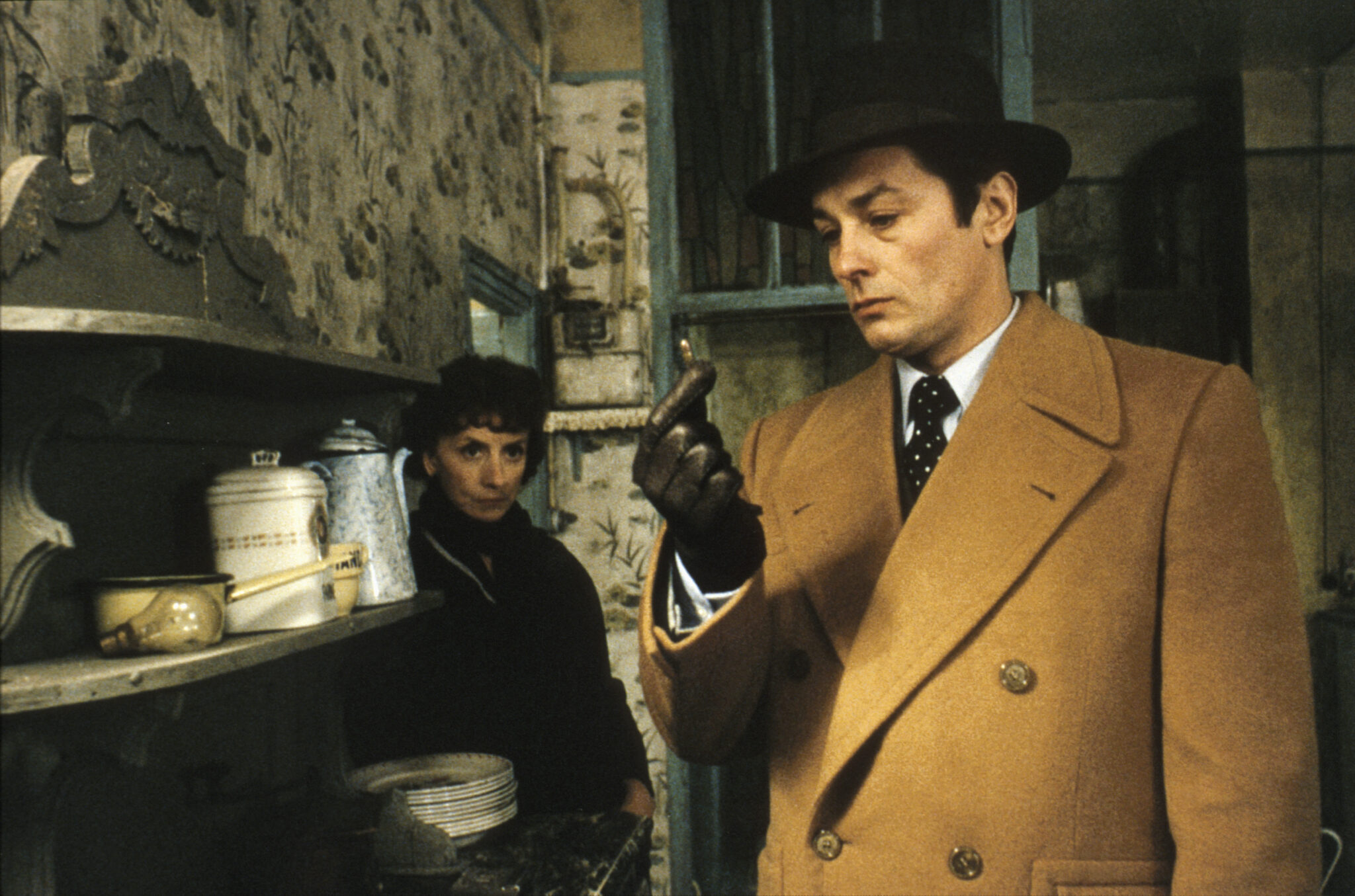 Robert Klein (Alain Delon) betrachtet in Monsieur Klein eine Patrone. Hinter ihm steht die Vermieterin seines vermeintlichen Doppelgängers.