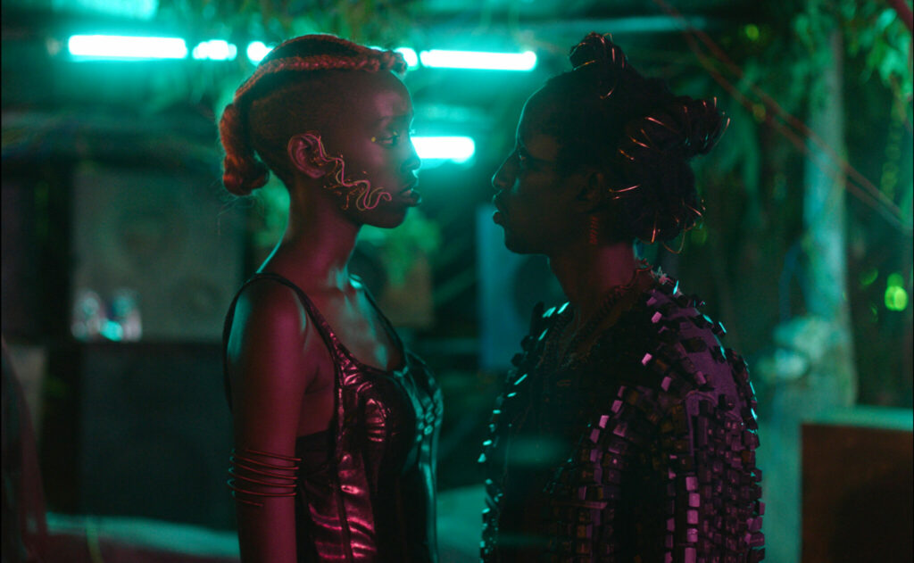 Zwei schwarze Frauen stehen sich gegenüber und schauen sich an. Beide haben viel Schmuck im Gesicht und verzierte Frisuren. Im Film Neptune Frost.