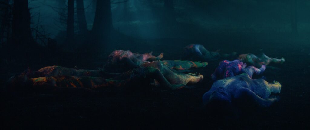 Im Film Nightsiren sind während eines nächtlichen Drogenrauschs neonfarbene, zuckende und nackte Leiber auf dem Waldboden zu sehen.