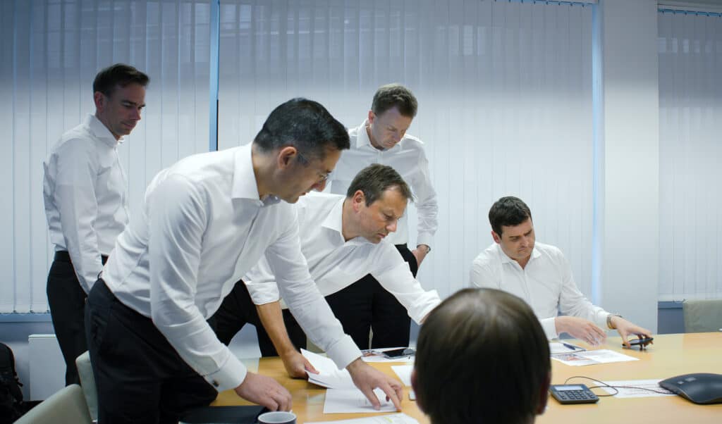 Investment-Banker in weißen Hemden disskutieren über einem Holztisch und schauen auf die ihnen vorliegenden Unterlagen