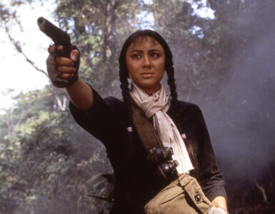 Sue (Joyce Godenzi) hält in Operation Eastern Condors mit ernstem Blick eine Pistole in der rechten Hand und visiert ein Ziel an.