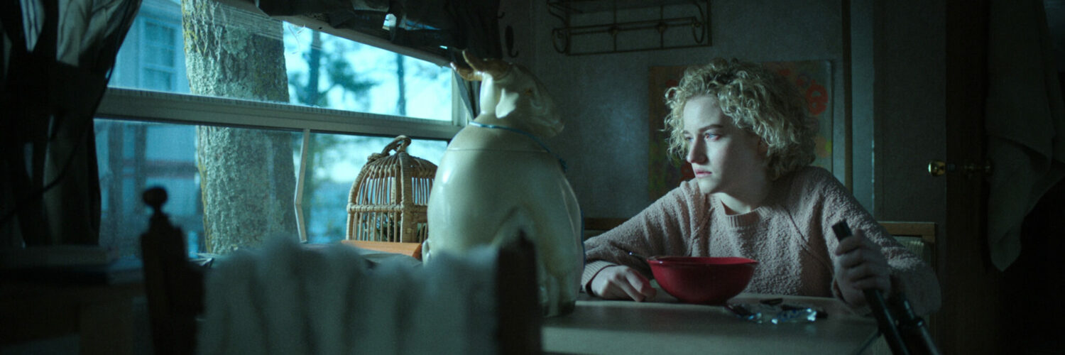 Ruth Langmore an einem Tisch in einem Wohnwagen mit Blick aus dem kleinen Fenster.