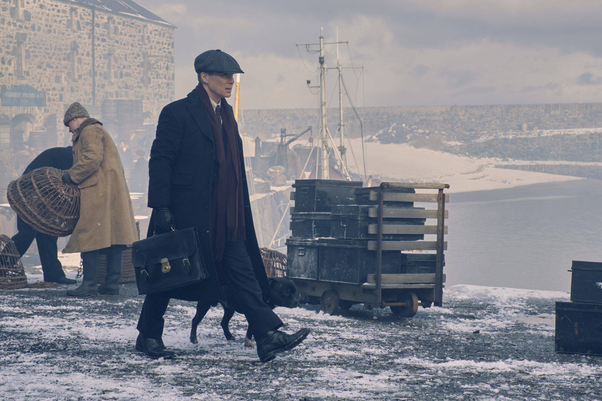 Auf dem Bild sieht man einen wandelnden Tommy Shelby am Hafen in Begleitung eines Hundes - Peaky Blinders