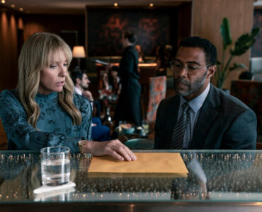 Toni Collette neben Omari Hardwick an einer Theke in einem Hotel. Beide blicken auf den Tresen vor ihnen.