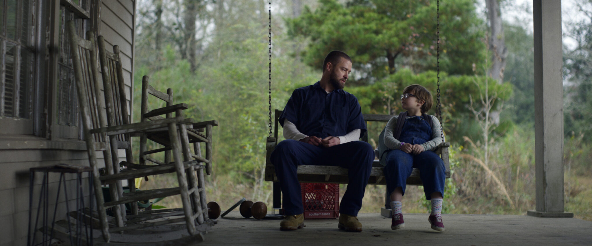 Justin Timberlake zusammen mit einem kleinen Jungen auf einer Schaukel sitzend auf einer Veranda.