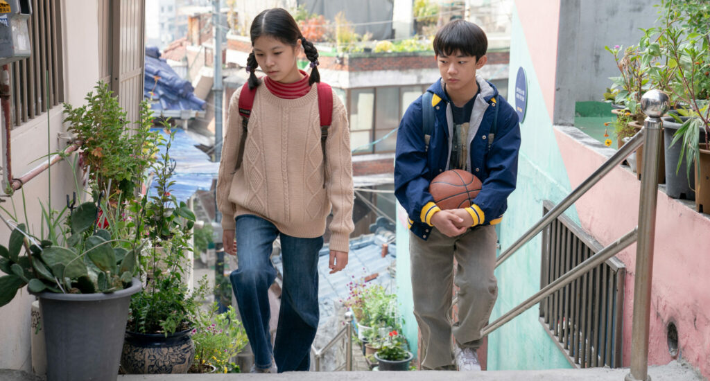 Die beiden Kindern Nora und Hae-sung gehen nebeneinander eine Treppe in Seoul hoch