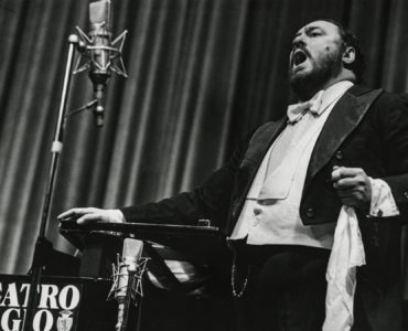 Pavarotti singt im Stehen inbrünstig eines seiner ausgewählten Stücke. Das Bild ist in Schwarz-Weiß gehalten.