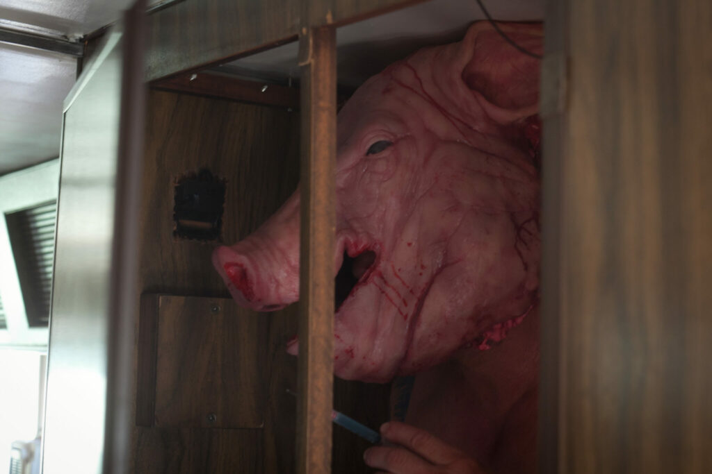Im Film Pig Killer ist Jake Busey als Willy Pickmann mit einer Schweinemaske auf dem Kopf tragend zu sehen. Mit nacktem Oberkörper steht er im Türrahmen seines Wohnwagens.