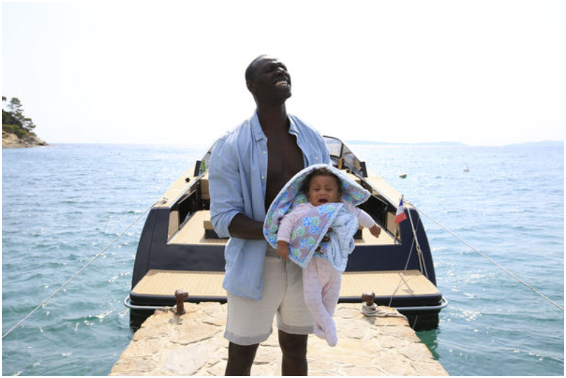 Plötzlich Papa - Omar Sy steht auf einem Bootsteg am Meer und hält sein Baby in Händen