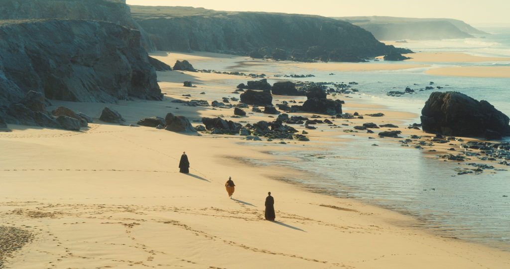 Marianne, Héloïse und ihre Freundin Sophie wandern am Strand. Sophie rennt dabei zwischen den beiden Frauen umher. Es ist teil eines wichtigen Rituals. | Porträt einer jungen Frau in Flammen