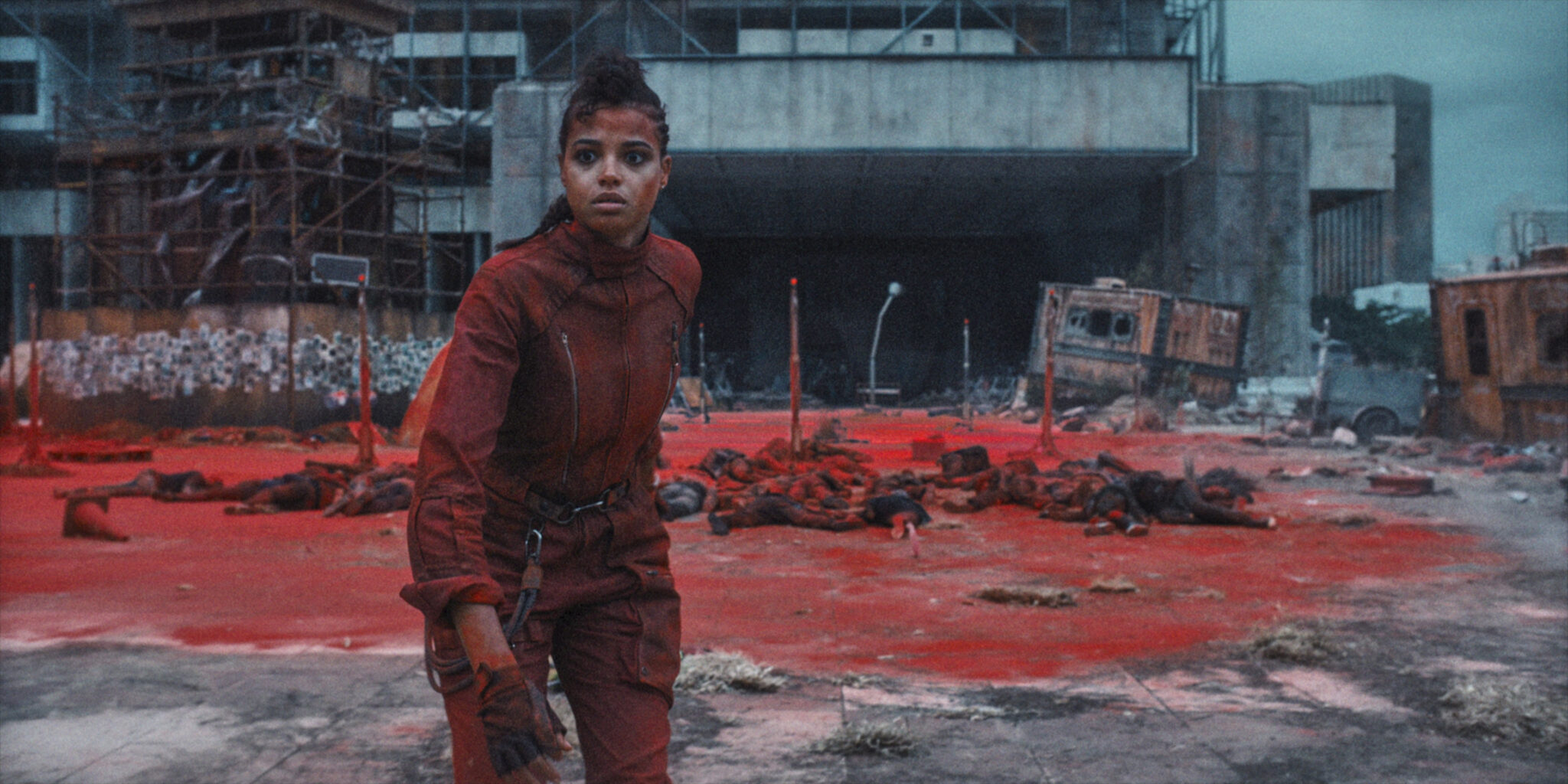 Ella Balinska steht schockiert in den Ruinen einer Großstadt, hinter ihr sehen wir Blut und Leichenteile von Infizierten - Resident Evil 2022