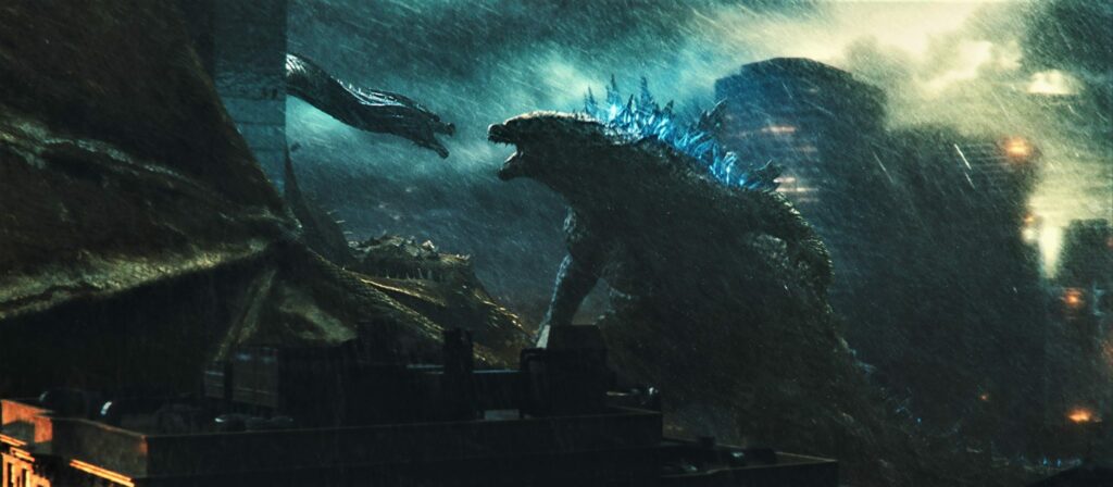 Das Bild zeigt eine Szene aus dem Film "Godzilla 2: King of the Monsters", wo sich die titelgebende Riesenechse Godzilla und der dreiköpfige Drache Ghidorah zu sehen, die sich vor einem malerischen Hintergrund anfauchen - Neu bei Prime im Juli 2022