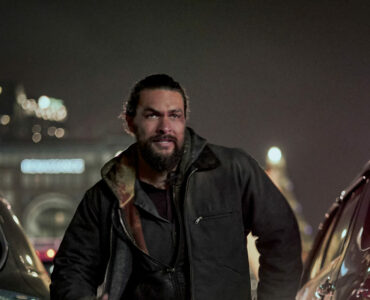 Jason Momoa als Ray Cooper nachts zwischen zwei Autos auf offener Straße. Im Hintergrund Hochhäuser.