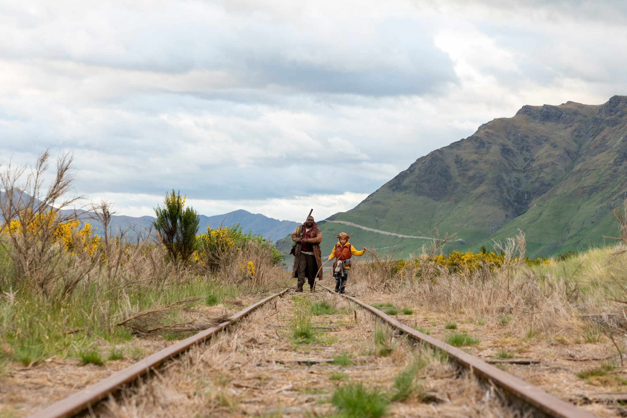 Tommy Jepperd (Nonso Anozie) und Gus (Christian Convery) laufen nebeneinander auf einem stillgelegten Gleis durch die Landschaft. Im Hintergrund sieht man ein Gebirge. Jepperd trägt ein Gewehr und Gus hält zwei Stöcke in den Händen.