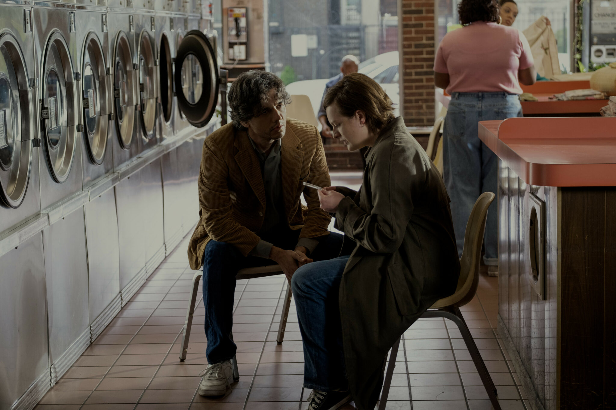 Wagner Moura sitzt neben Elizabeth Moss in einem Waschsalon. Die beiden unterhalten sich während sie einen Notizzettel vor sich hält. Shining Girls