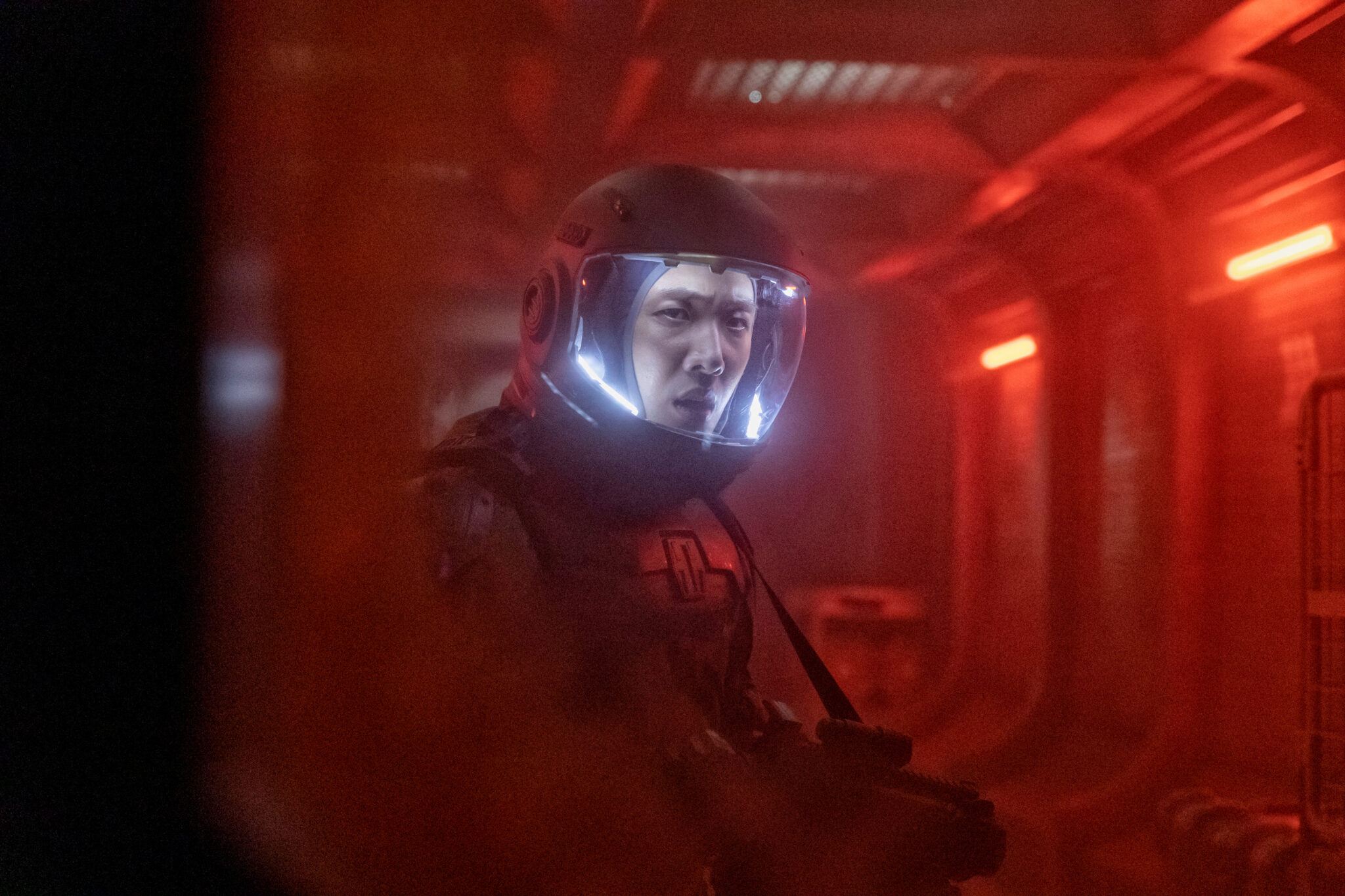 Ein Astronaut in einer rotbeleuchteten Raumstation mit ernsten Blick unter seinem Helm.