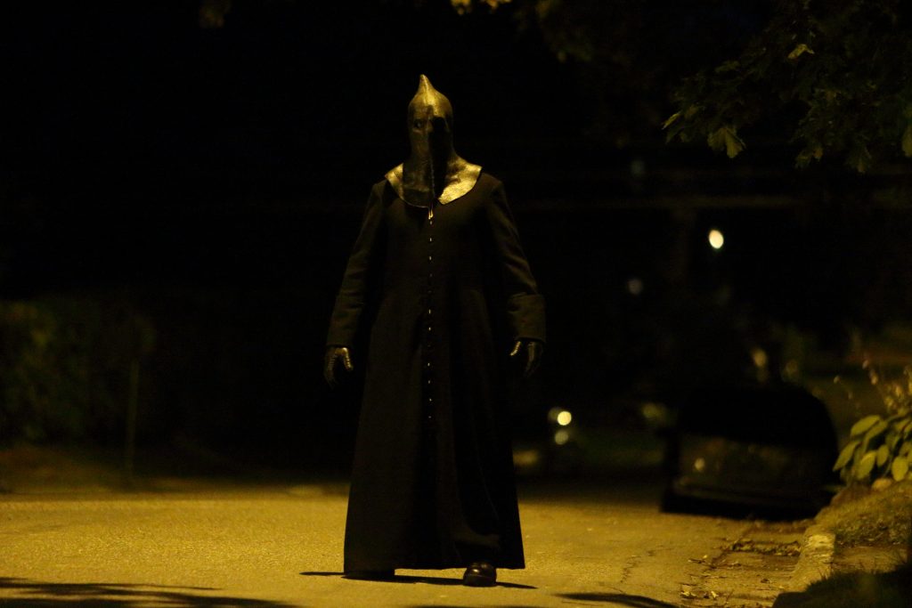 Nachts auf der Straße steht ein Mann im schwarzen Gewand mit Maske in Slasher - Season 1