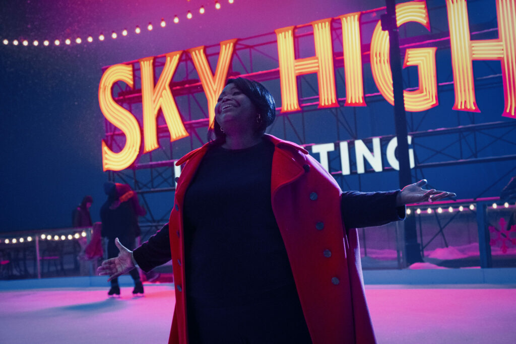 Kimberly steht auf einer Eisfläche und singt. Hinter ihr ist ein Neonschild angebracht, welches die Wörter "Sky High" darstellt