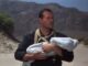 Robert, gespielt von John Wayne, hält das Baby etwas hilflos im Arm.